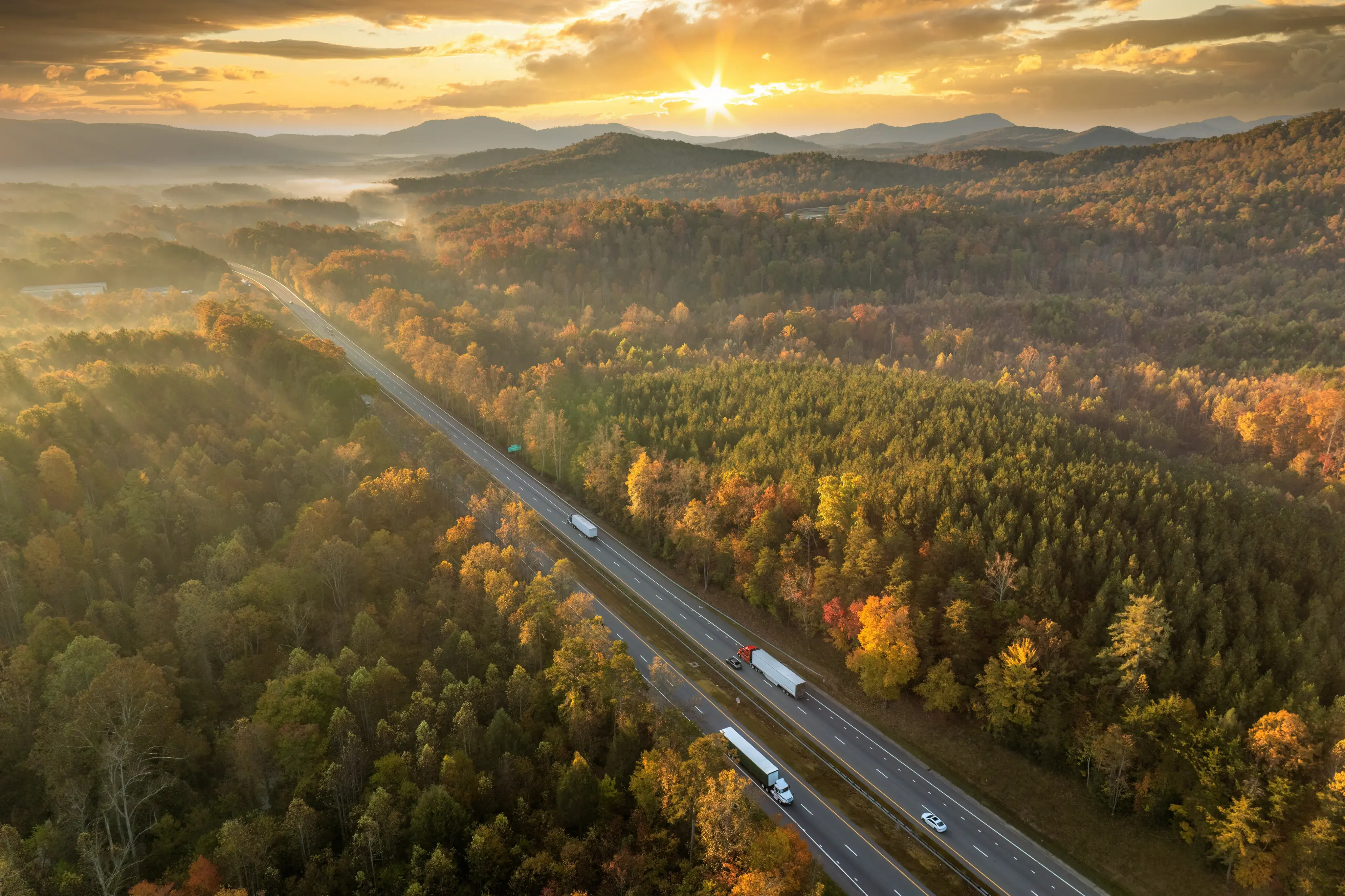 Aerial view of highway winding through forested hills with trucks in motion