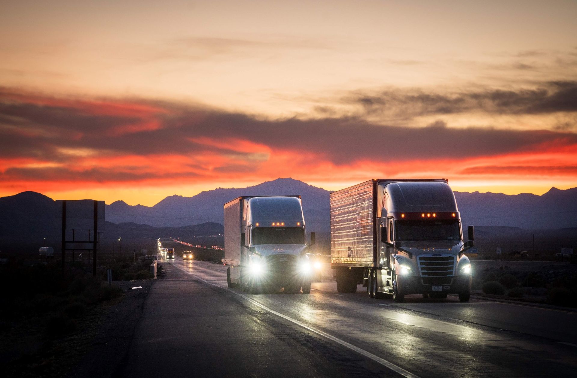 Multiple semi trucks driving toward the camera on a highway at golden hour